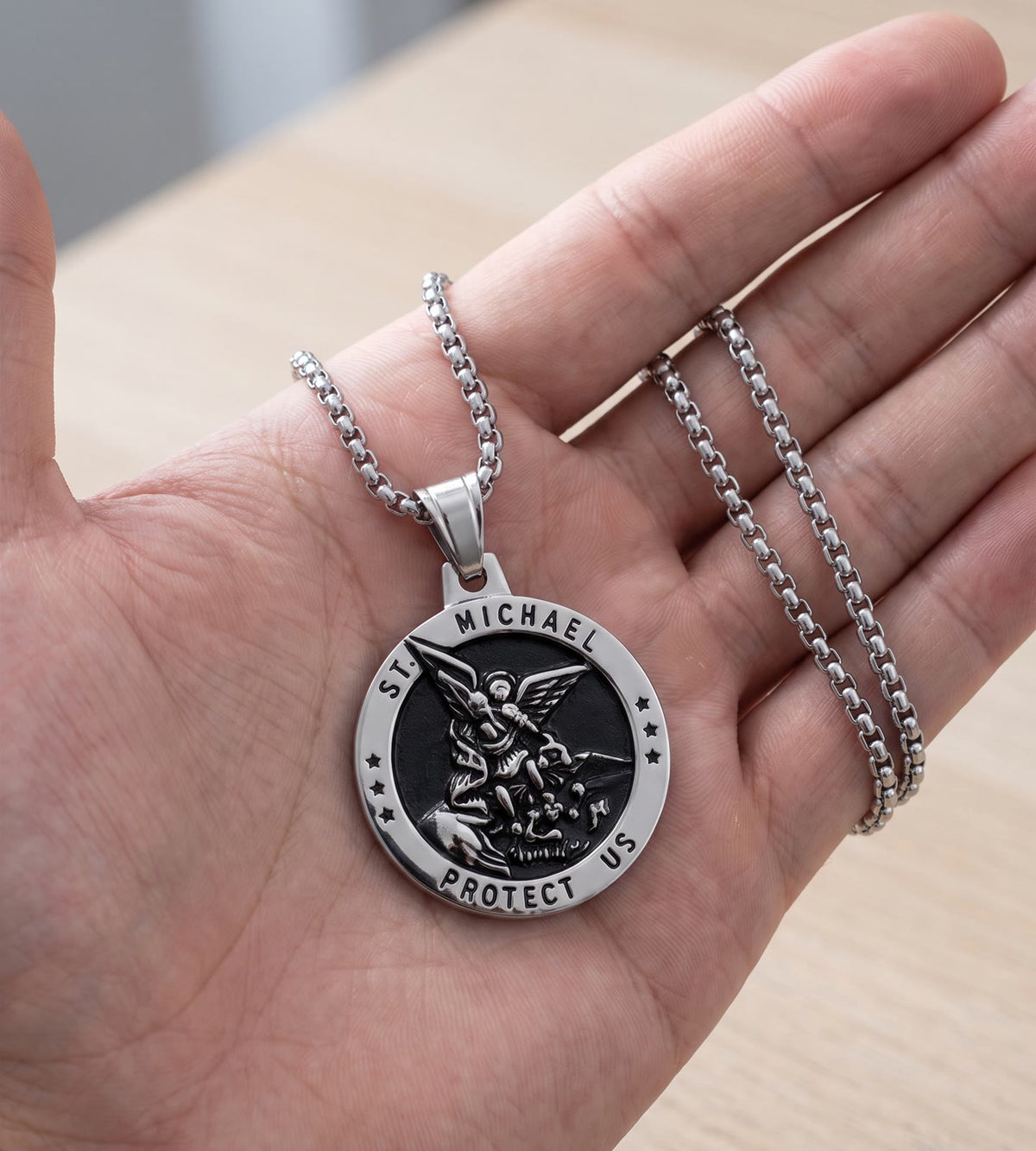The silver St Michael medal in a man’s open palm, the box chain over his fingers