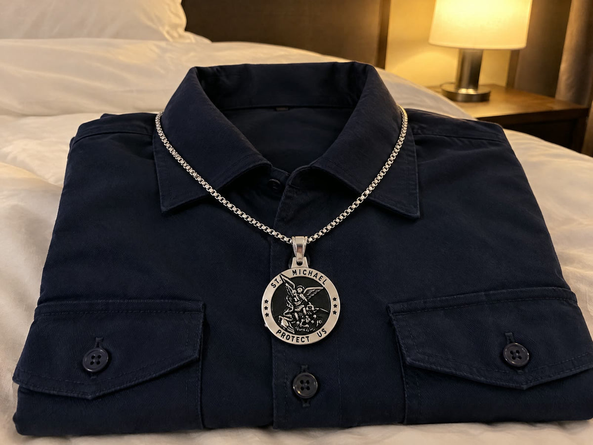A folded navy uniform shirt on a hotel bed with a silver St Michael medal laid on it