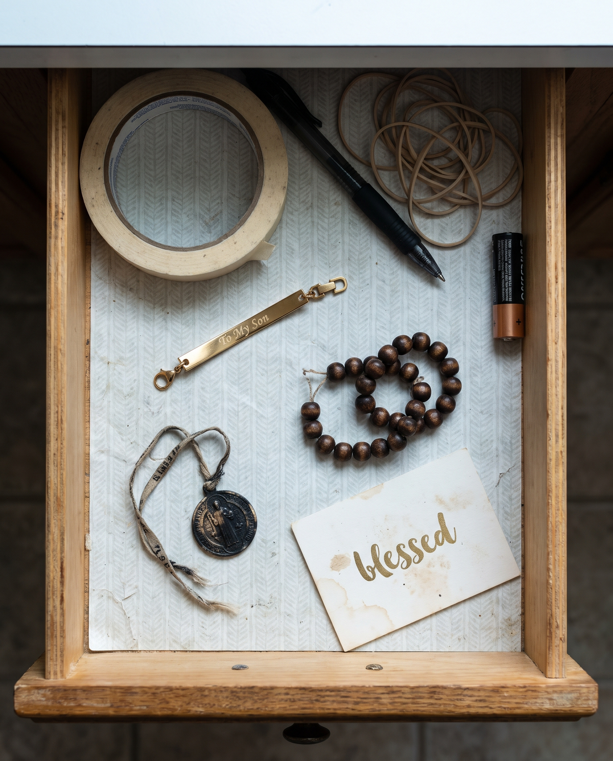 An open kitchen drawer with a snapped bar bracelet, a blackened medal and broken wooden beads