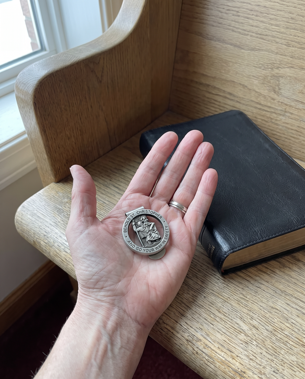 The St Christopher visor clip in a woman’s palm over a church pew