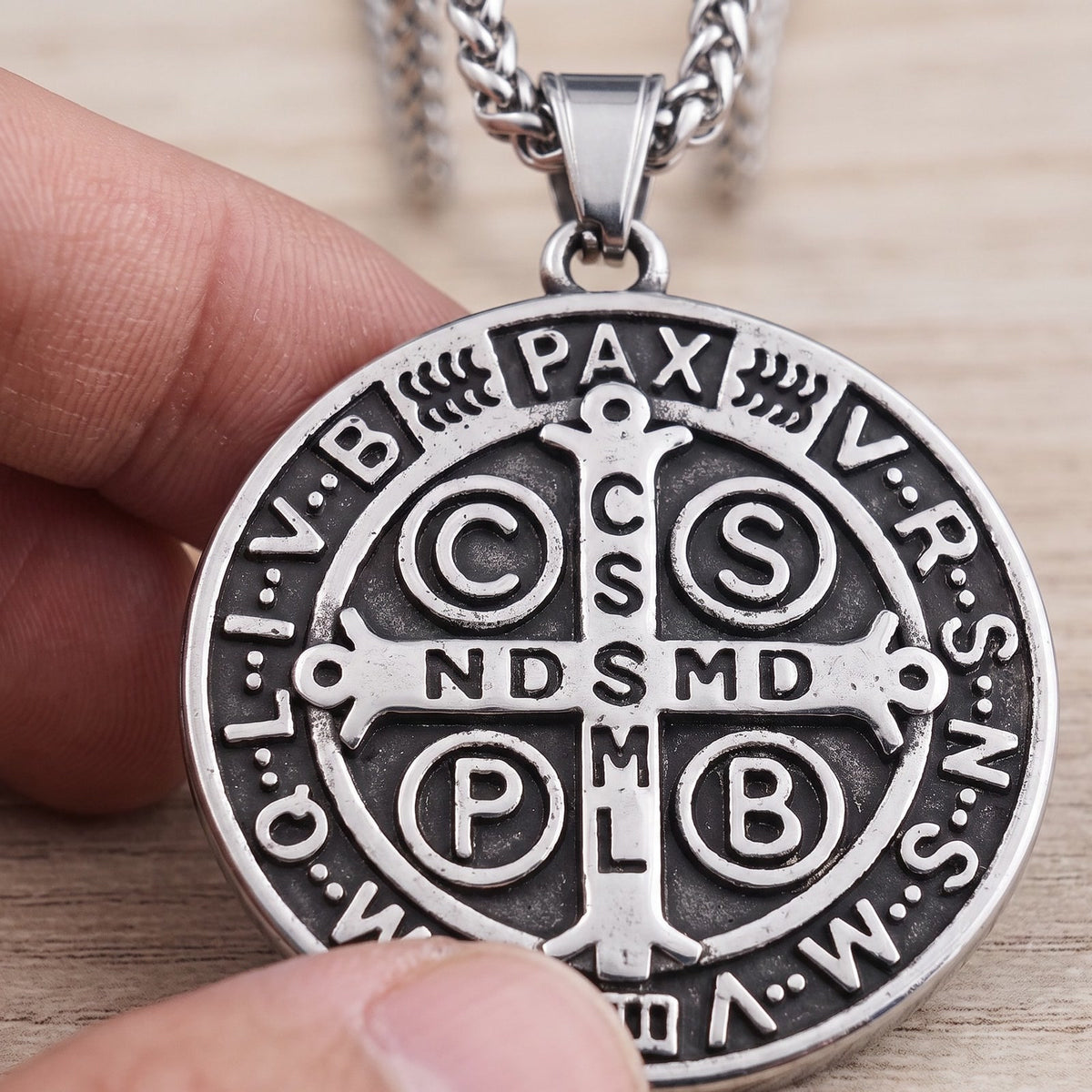 The St Benedict medal’s cross side, close up, every letter sharp under a thumb