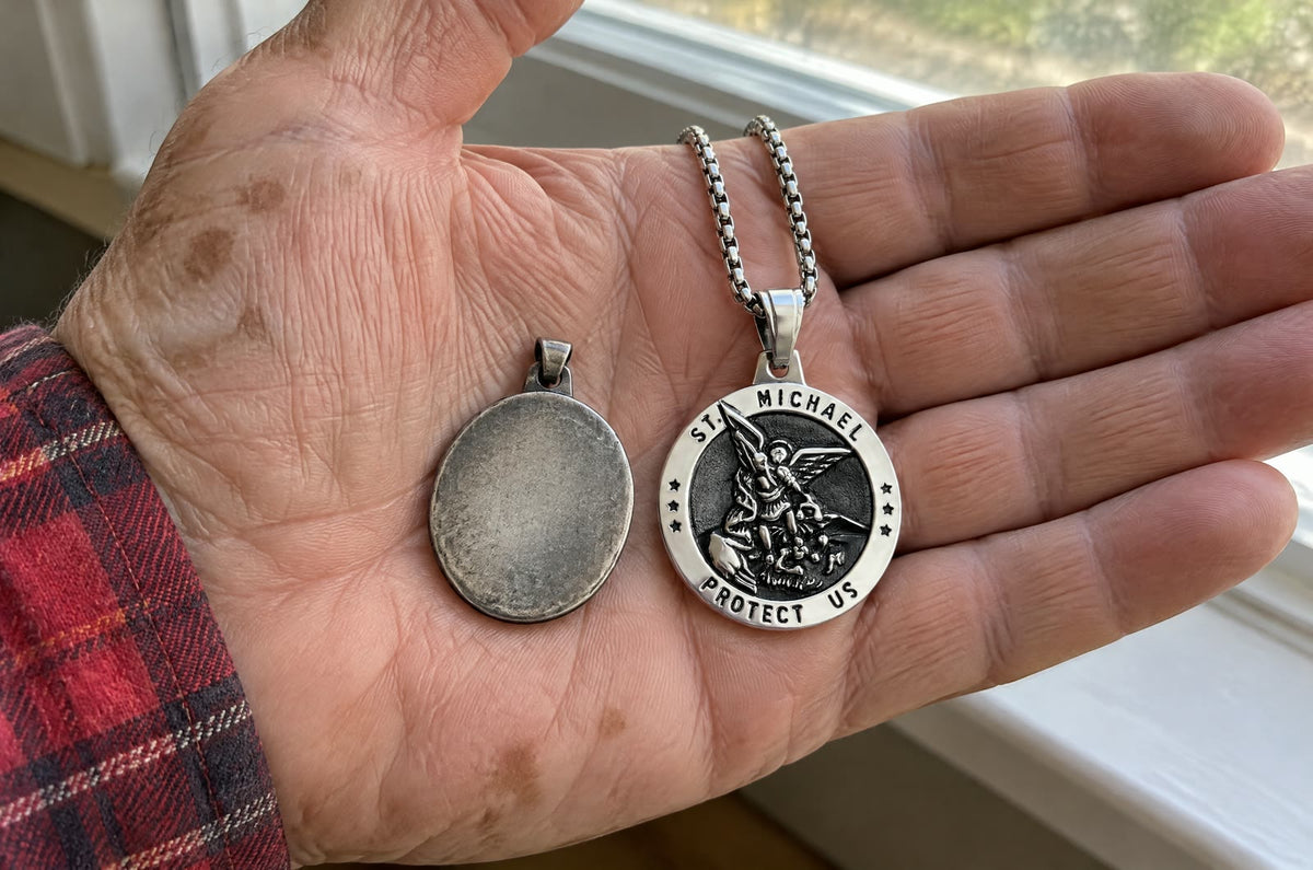 An old man’s open palm holding a worn-smooth grey medal beside a new silver St Michael medal