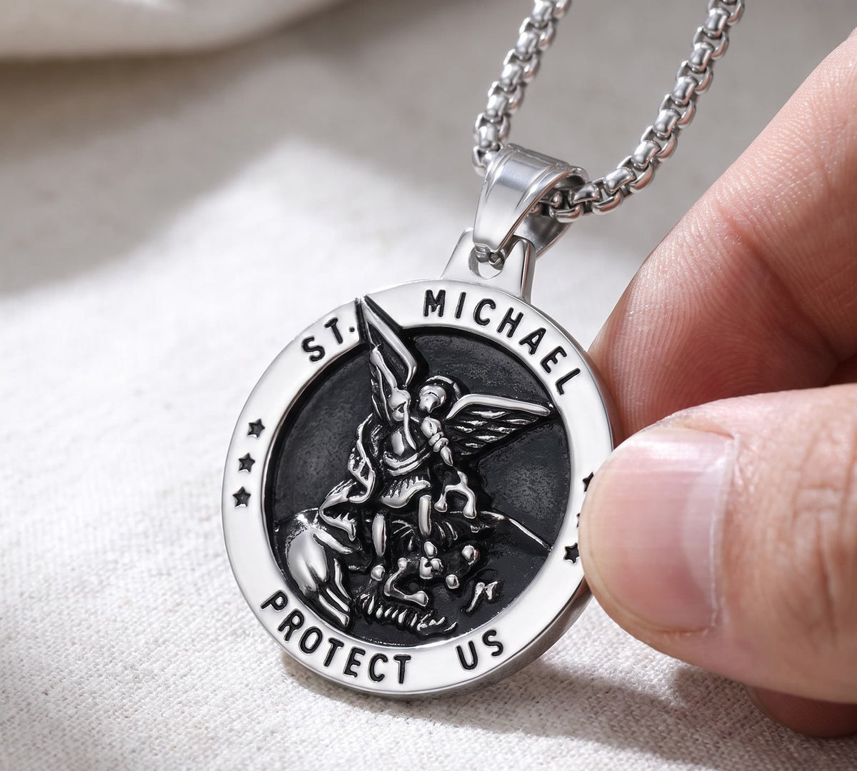 The silver St Michael medal between a thumb and a finger, ST. MICHAEL and PROTECT US sharp on the rim