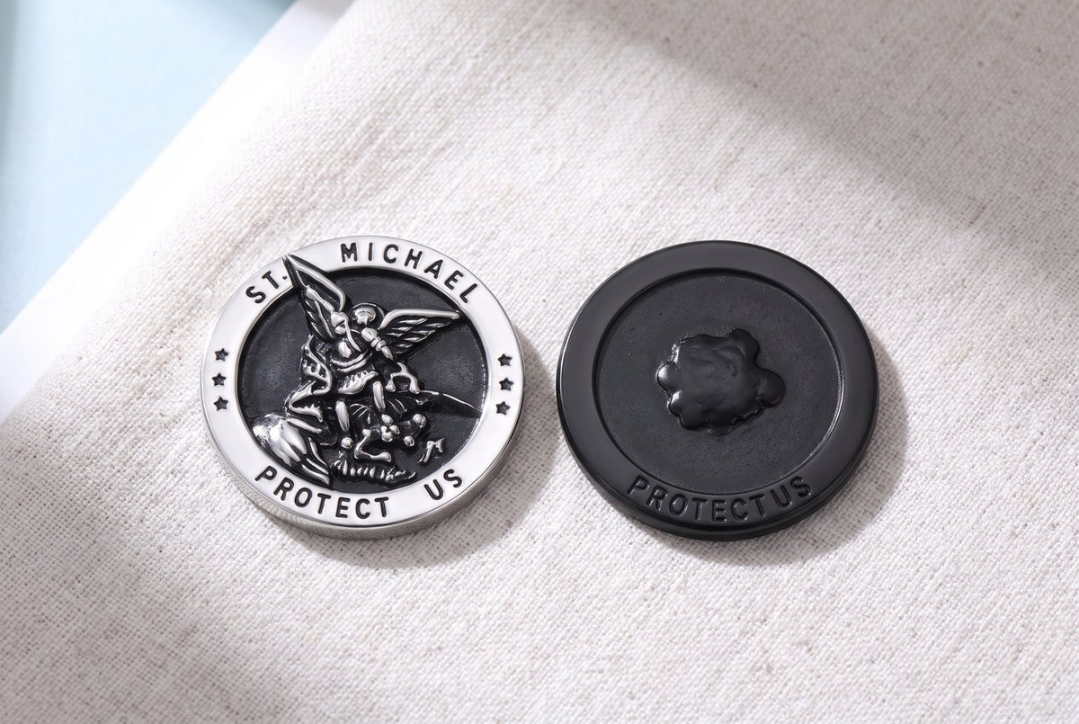 The St Michael medal beside a flat black store medal on linen, one rim reading PROTECT US, the other a dark disc reading PROTECTUS