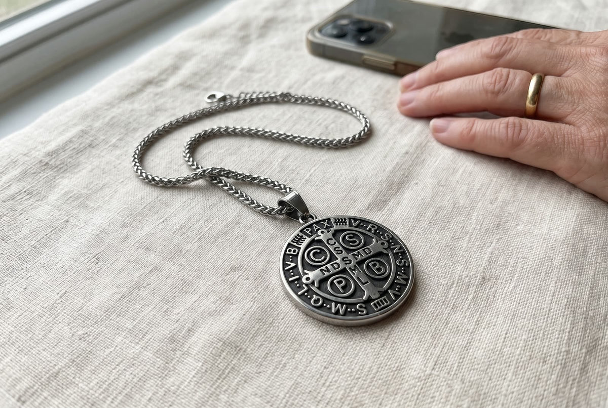 The St Benedict medal on its chain on linen beside a woman’s hand and her phone
