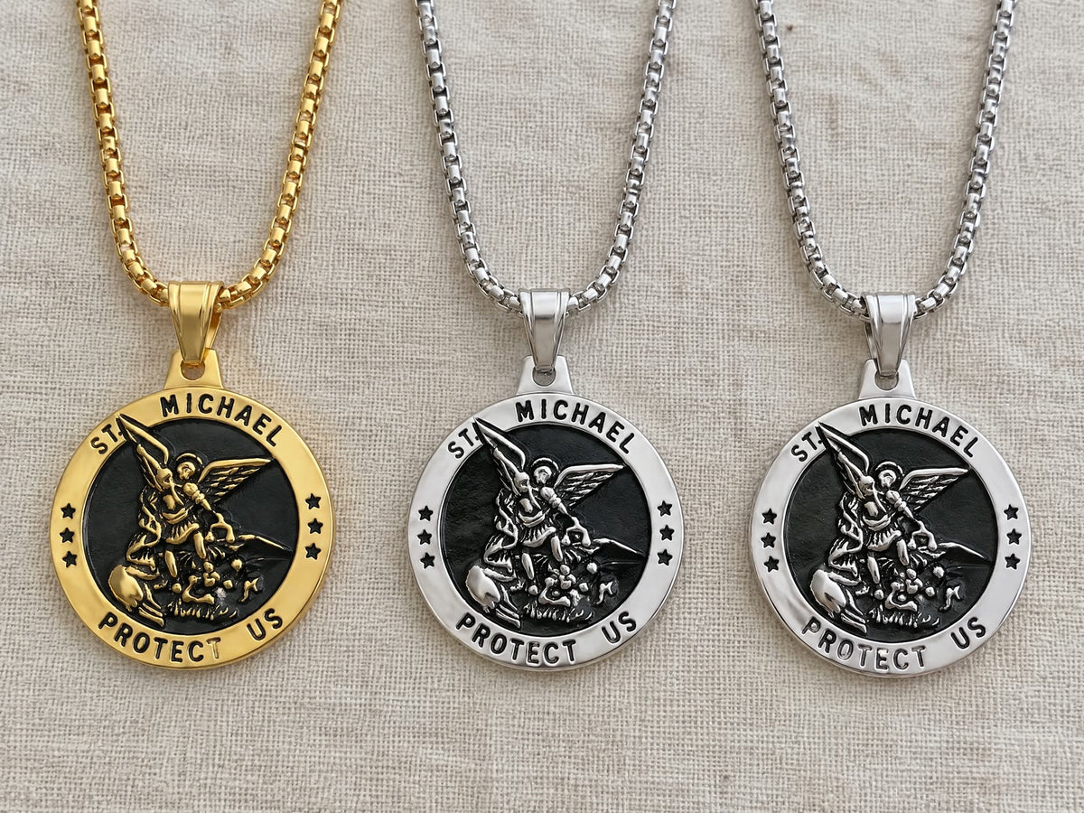Three St Michael medals, one gold and two silver, on their box chains on plain linen