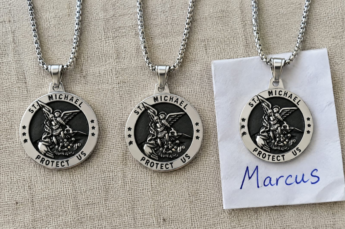 Three silver St Michael medals on linen, the third on a square of notepaper with Marcus handwritten in blue ink