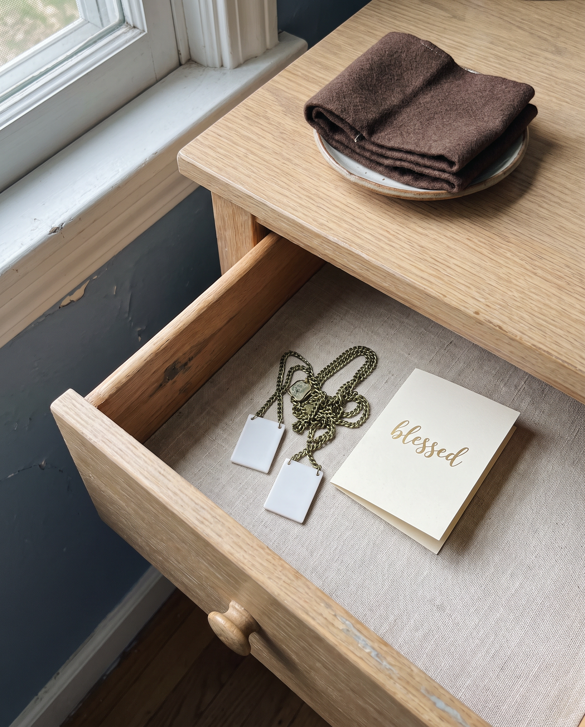 An open dresser drawer with a plastic scapular necklace and a chain gone green, a cloth scapular beside it