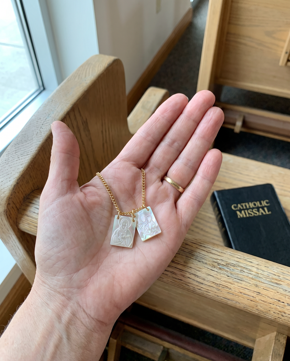 The mother-of-pearl scapular in a woman’s palm over a church pew